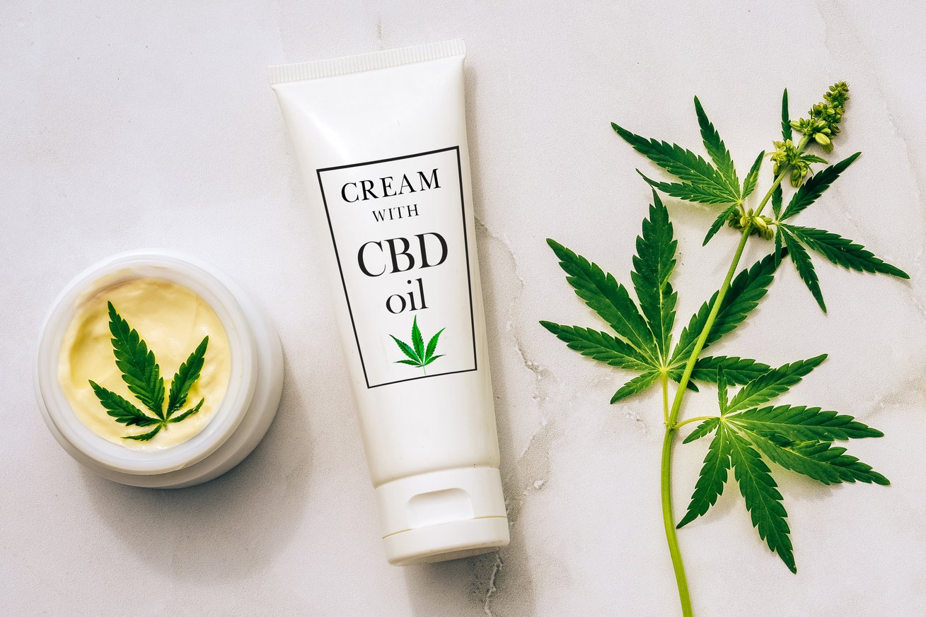 Cream with CBD Oil and Cannabis Leaves on White Table